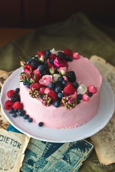 a pink cake topped with berries and blueberries on top of a white platter