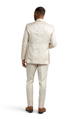 A slim ivory paisley tuxedo coat with one button and a shawl lapel. Fitted Cream Nehru Jacket For Formal Occasions, Elegant Beige Nehru Jacket With Long Sleeves, Elegant Beige Tuxedo With Notch Lapel, Beige Notch Lapel Outerwear For Wedding, Beige Long Sleeve Nehru Jacket For Formal Occasions, Cream Fitted Nehru Jacket For Semi-formal Occasions, Fitted Elegant Nehru Jacket For Semi-formal Occasions, Elegant Beige Tuxedo For Groom, Tailored Cream Outerwear For Wedding