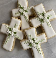 decorated cookies in the shape of crosses with white flowers and green leaves are on a table