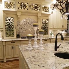 a large kitchen with marble counter tops and white cabinets, chandelier above the sink