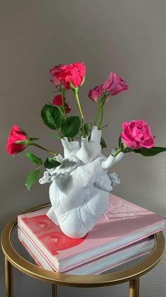 a vase filled with pink roses sitting on top of a table next to a stack of books