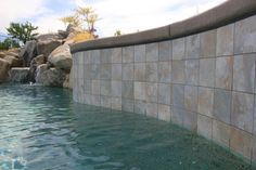 there is a pool with water and rocks in the backround, next to a rock waterfall