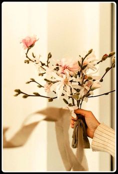 a person holding a bouquet of flowers in their hand and ribbon around the vase with it