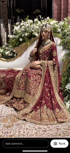 a woman in a red and gold wedding dress sitting on a couch with flowers behind her