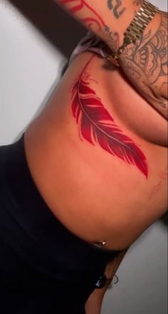 a woman with tattoos on her stomach has a red feather tattoo