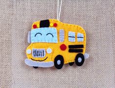 a yellow school bus ornament hanging from a string on a tan fabric background