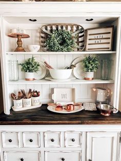 a white hutch filled with lots of dishes and greenery on top of it