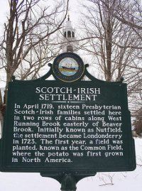 a sign in front of some trees and snow on the ground, with a clock tower in the background