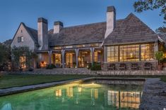 a large house sitting next to a pond in front of a lush green yard with trees