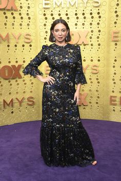 a woman in a black dress standing on a purple carpet with her hands on her hips