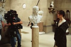 a cameraman filming a woman in front of a busturine and other statues