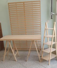 three wooden ladders are standing next to a table and shelf in a room with light blue walls