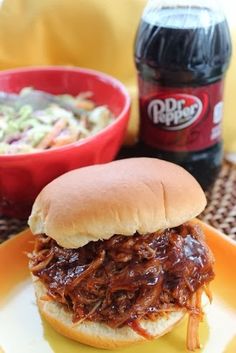 a pulled pork sandwich on a bun with coleslaw and soda in the background