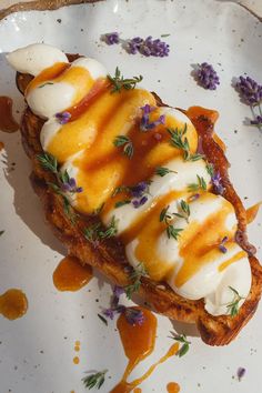 a white plate topped with an open face sandwich covered in cheese and sauce next to purple flowers