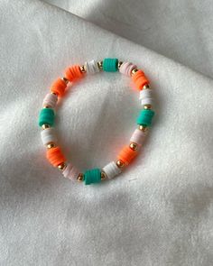 an orange, white and green beaded bracelet on top of a white cloth covered surface