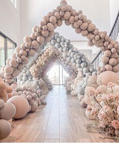 an arch made out of balloons and flowers on the floor in front of a staircase