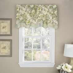 there is a window with flowers on the valance and two framed pictures above it