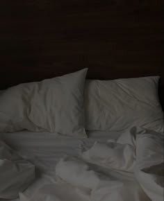 an unmade bed with white sheets and pillows