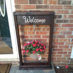 a welcome sign hanging on the side of a brick building with flowers in front of it