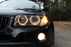 the front end of a black car with its lights on and headlamps down