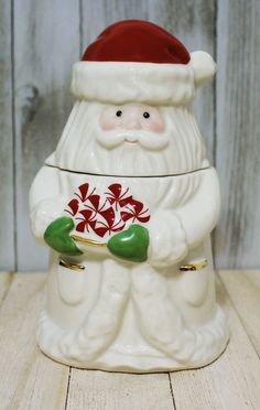 a santa claus cookie jar with candy canes in his hands on a wooden table