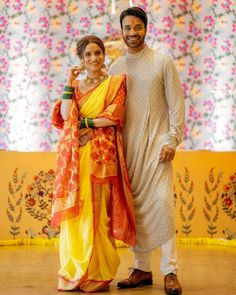 a man and woman standing next to each other in front of a wall with flowers