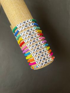 several bracelets with letters on them hanging from a wooden pole in front of a gray wall