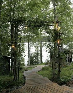 a wooden walkway in the woods leading to a lake with trees and lights on it