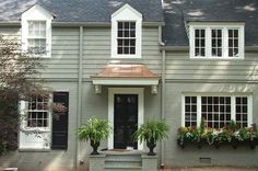 a gray house with white windows and plants on the front porch in front of it