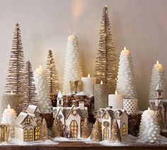 a group of small christmas trees sitting on top of a table next to candles and snow covered houses