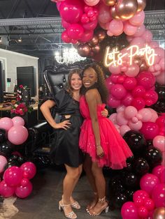 two women standing next to each other in front of pink and black balloons at a party