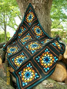 a crocheted blanket sitting on top of a pile of logs next to a tree