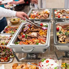 people are serving themselves food at a buffet