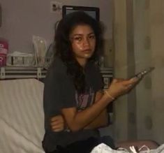 a woman sitting on top of a bed holding a remote control