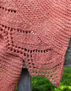 a pink crocheted shawl draped over a wooden fence