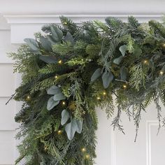 a christmas wreath with lights and greenery hanging from the front door, on a white wall