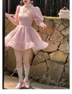 a woman wearing a pink dress and white shoes standing in front of a stone wall