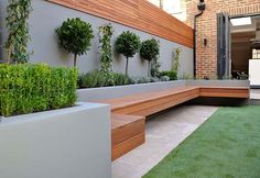 an outdoor garden with wooden benches and green plants on the wall, along with artificial grass