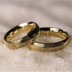 two gold wedding bands with fingerprints on them sitting in the snow, close up