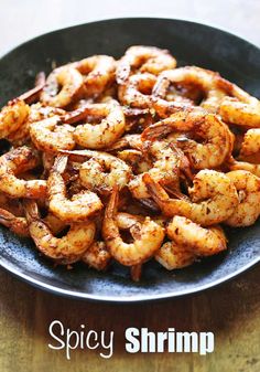 a plate full of shrimp sitting on top of a wooden table with the words spicy shrimp over it