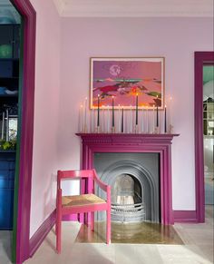 a room with pink walls and a purple chair in front of a fire place that has candles on it