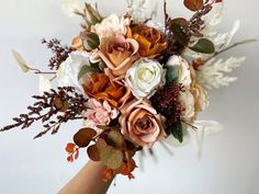 a bridal bouquet with white and peach flowers on the top is held by a woman's hand