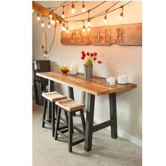 a wooden table with two stools and flowers on it in front of a wall