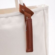 a white tote bag with a brown handle and leather strap hanging from the side