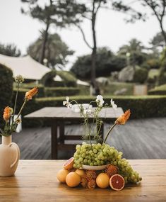 a table topped with fruit and flowers next to a vase on top of a wooden table