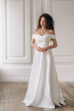 a woman wearing a white wedding dress standing in front of an empty wall with her hands on her hips