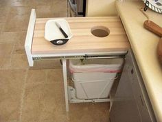 a kitchen counter with a cutting board on it and a trash can under the sink