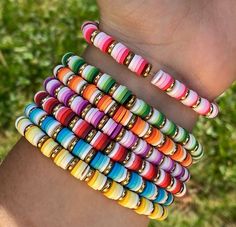 a woman's arm with several different colored bracelets on her wrist and one is holding