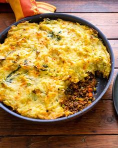 an omelet with meat and vegetables in a pan on a wooden table next to a fork