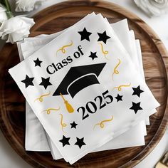 four graduation paper napkins on top of a wooden plate with white flowers and gold confetti